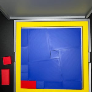 May include: A blue puzzle with 12 pieces in a gray box with a yellow border. There are three red pieces outside the box.
