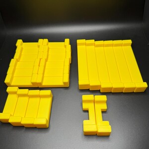 May include: A set of four yellow building blocks, made of plastic. The blocks are in different sizes and shapes, and can be used to build towers, walls, or other structures.
