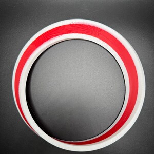 May include: A white circular object with a red stripe around the center. The object is a ring shape, with a smooth, clean finish. The background is a solid black color.