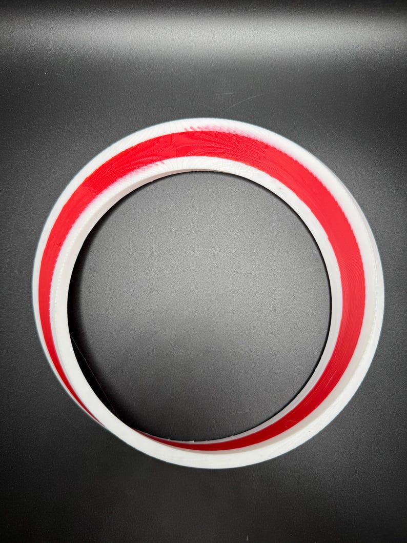 May include: A white circular object with a red stripe around the center. The object is a ring shape, with a smooth, clean finish. The background is a solid black color.