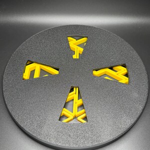 May include: A black round disc with a yellow geometric design cut out of the center. The design is a four-pointed star with a zig-zag pattern.
