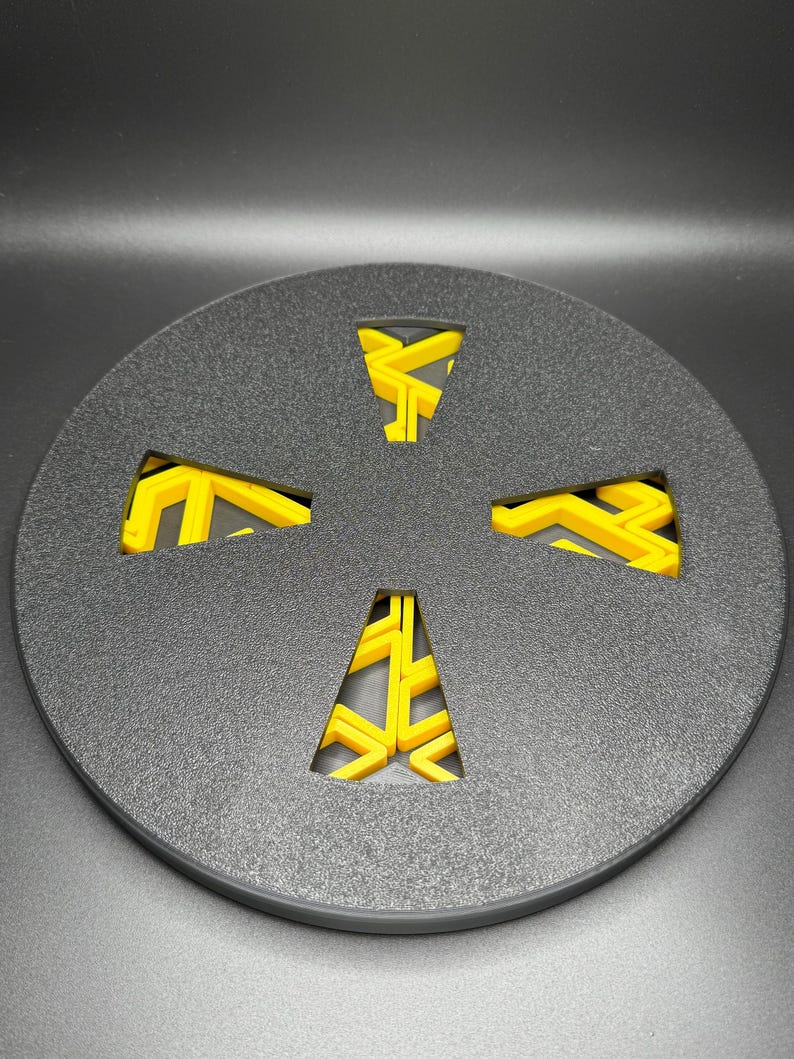 May include: A black round disc with a yellow geometric design cut out of the center. The design is a four-pointed star with a zig-zag pattern.