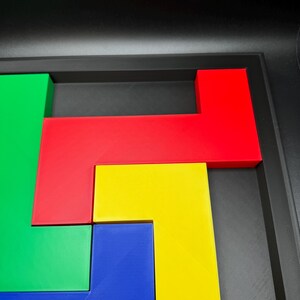 Op de afbeelding: Een kleurrijk puzzelspel met geometrische vormen in rood, groen, geel en blauw. De stukken zijn gerangschikt in een zwarte bak, wat een levendige en aantrekkelijke uitstraling cre&euml;ert. De puzzel is ontworpen voor ruimtelijk inzicht en probleemoplossing.