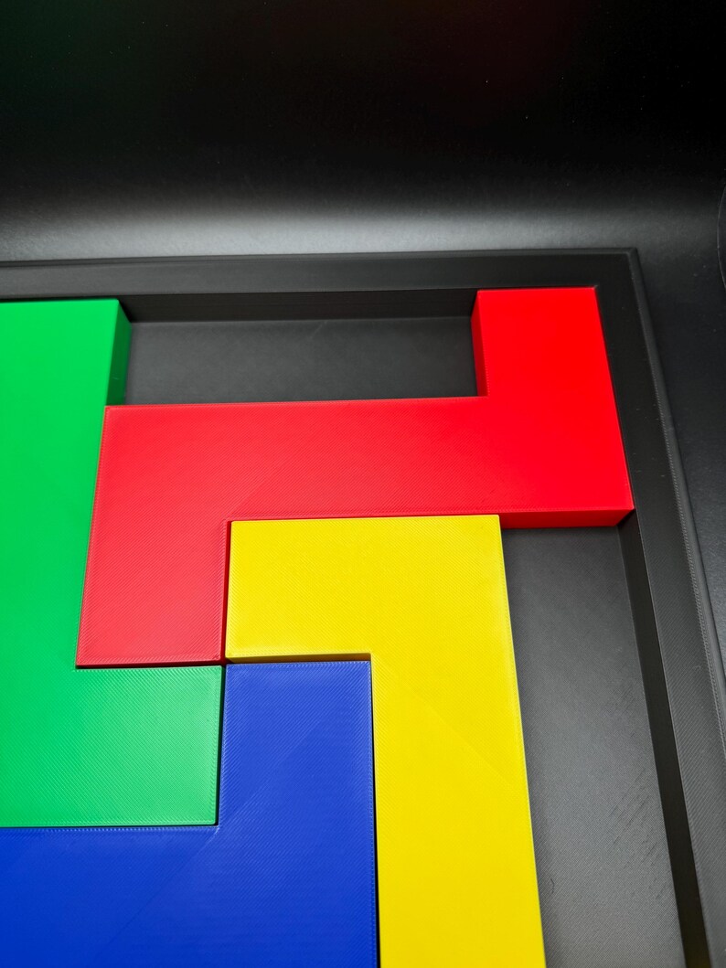Op de afbeelding: Een kleurrijk puzzelspel met geometrische vormen in rood, groen, geel en blauw. De stukken zijn gerangschikt in een zwarte bak, wat een levendige en aantrekkelijke uitstraling cre&euml;ert. De puzzel is ontworpen voor ruimtelijk inzicht en probleemoplossing.