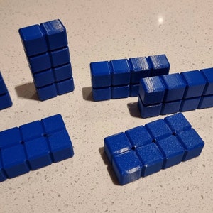 May include: Six blue building blocks made of small squares. The blocks are arranged in different configurations.