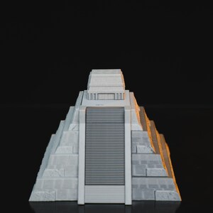 May include: A gray miniature model of a pyramid with a stepped design and a small structure on top. The pyramid is on a black surface.