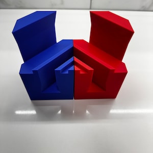 May include: Two geometric shapes, one blue and one red, are joined together. The shapes are made of a smooth, solid material and have a modern, abstract design.