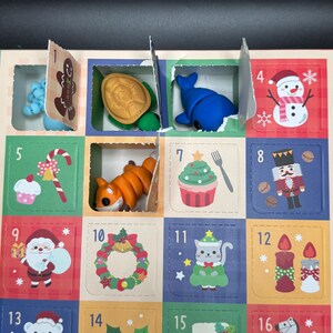May include: Advent calendar with numbered compartments, each revealing a small toy or decoration. Includes a gingerbread man, turtle, whale, snowman, fox, cupcake, nutcracker, Santa, wreath, cat, candles, polar bear, holly, stocking, and rocking horse.