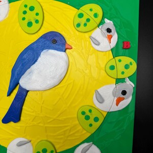 May include: A colorful puzzle featuring a blue bird, white birds, and green eggs on a yellow background. The puzzle pieces are arranged on a green surface, creating a vibrant and playful scene. The bird has a blue body, white chest, and orange beak.