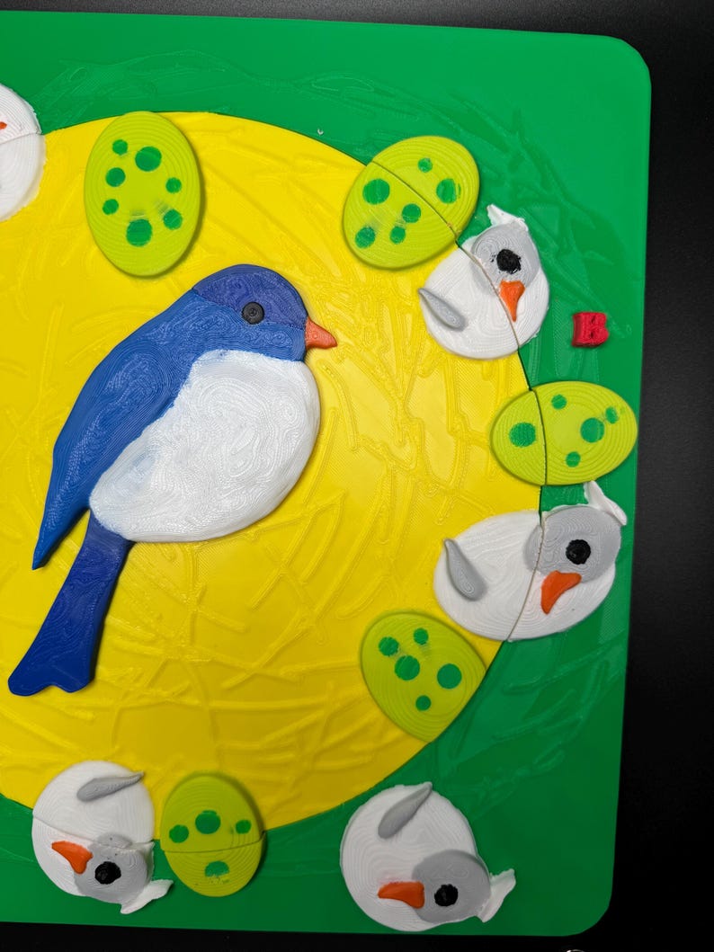 May include: A colorful puzzle featuring a blue bird, white birds, and green eggs on a yellow background. The puzzle pieces are arranged on a green surface, creating a vibrant and playful scene. The bird has a blue body, white chest, and orange beak.