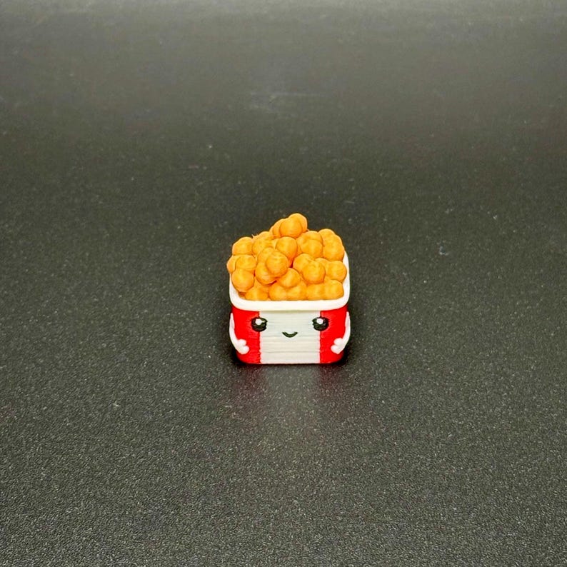 May include: A small, white, red, and orange 3D printed figurine of a cartoon bucket of fried chicken with a smiling face.