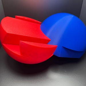 Puede incluir: Un rompecabezas 3D rojo y azul en forma de dos esferas que se entrelazan. El rompecabezas est&aacute; hecho de pl&aacute;stico y tiene un acabado liso.