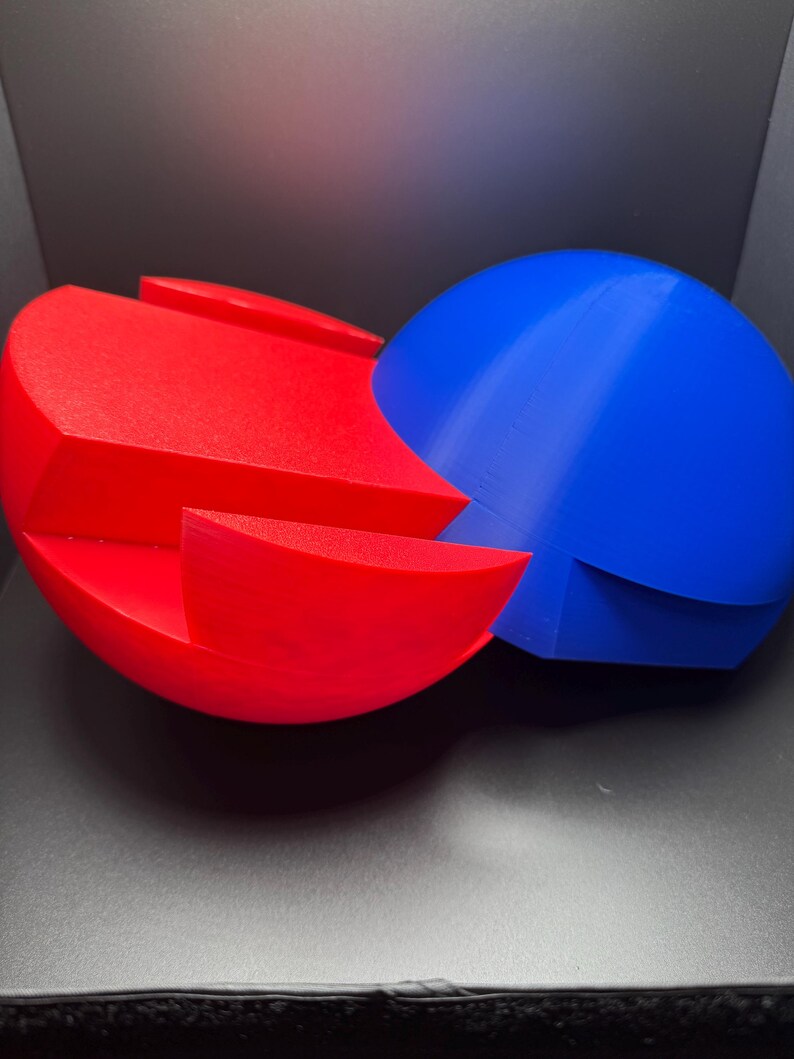 Puede incluir: Un rompecabezas 3D rojo y azul en forma de dos esferas que se entrelazan. El rompecabezas est&aacute; hecho de pl&aacute;stico y tiene un acabado liso.