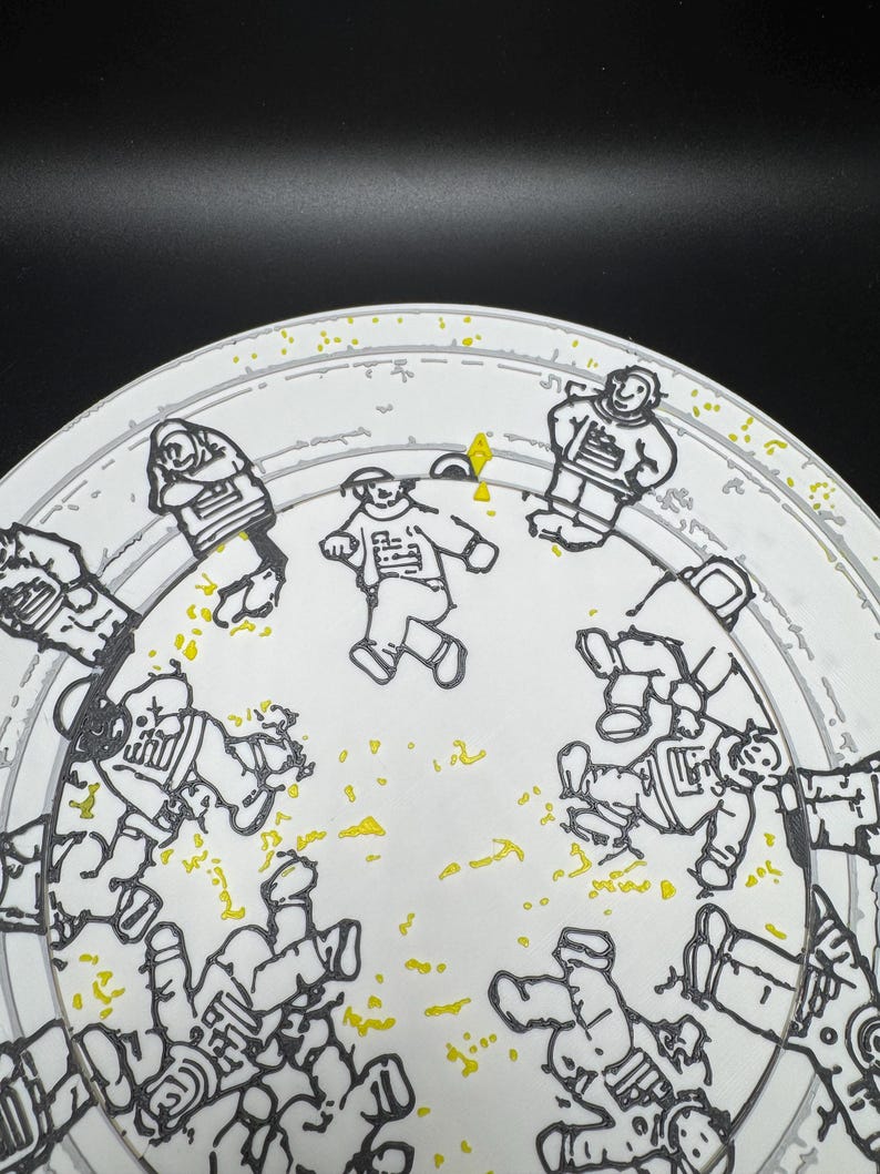 Puede incluir: Un plato blanco con una ilustraci&oacute;n en negro y amarillo de astronautas con trajes espaciales. Los astronautas est&aacute;n en varias poses, algunos de pie y otros flotando. El plato tiene un borde gris.