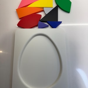 Op de afbeelding: Een witte, eivormige puzzel met een wit frame. De puzzelstukken zijn verspreid boven het frame en omvatten een verscheidenheid aan kleuren en vormen, waaronder rood, oranje, geel, groen, blauw, paars en zwart.
