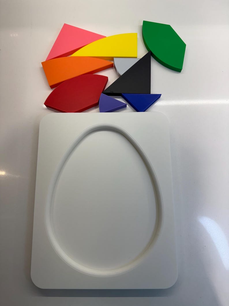 Op de afbeelding: Een witte, eivormige puzzel met een wit frame. De puzzelstukken zijn verspreid boven het frame en omvatten een verscheidenheid aan kleuren en vormen, waaronder rood, oranje, geel, groen, blauw, paars en zwart.