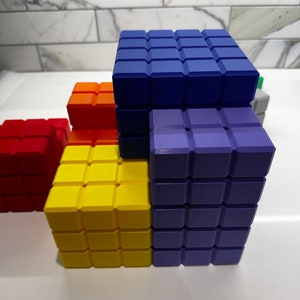 May include: A stack of colorful building blocks made of small squares. The blocks are blue, purple, yellow, orange, and red. The blocks are arranged in a staggered pattern.