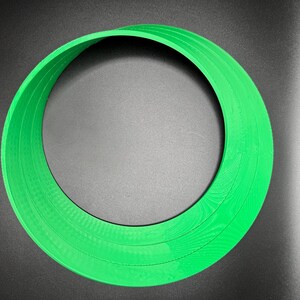 May include: A green plastic ring with multiple layers, creating a circular shape.