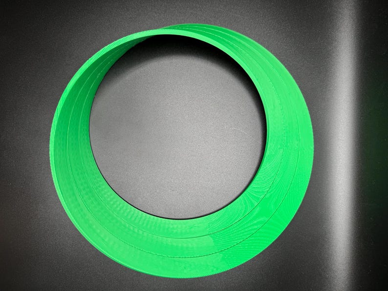 May include: A green plastic ring with multiple layers, creating a circular shape.