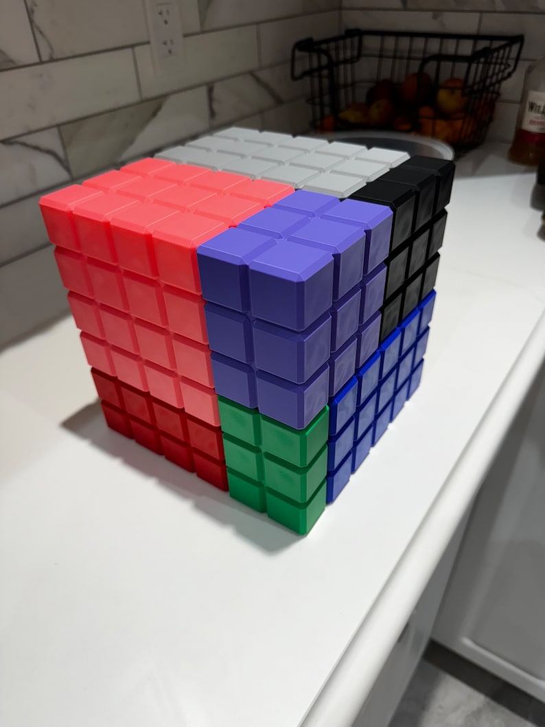 May include: A colorful cube puzzle made of small square blocks. The cube is made up of six different colors: red, purple, green, blue, black, and white.