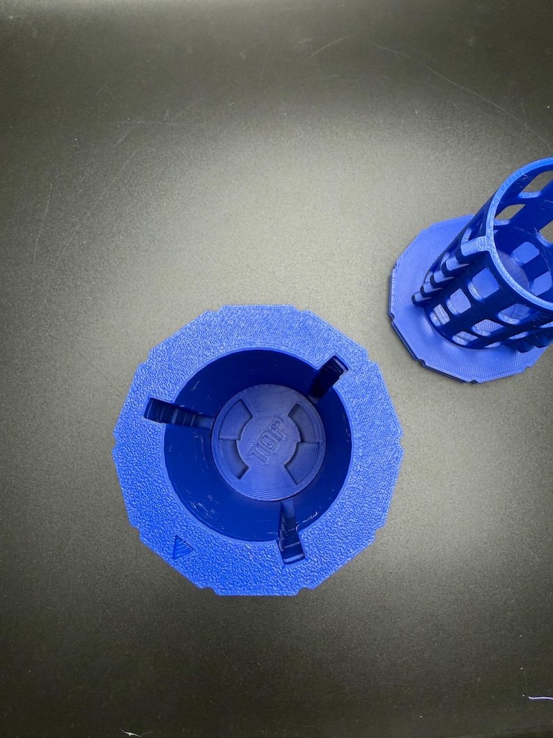 May include: Two blue, 3D-printed objects. One is a cylindrical cage with a hexagonal base. The other is a wider, hexagonal base with a central circular indentation. The word "TOP" is visible in the center of the base.