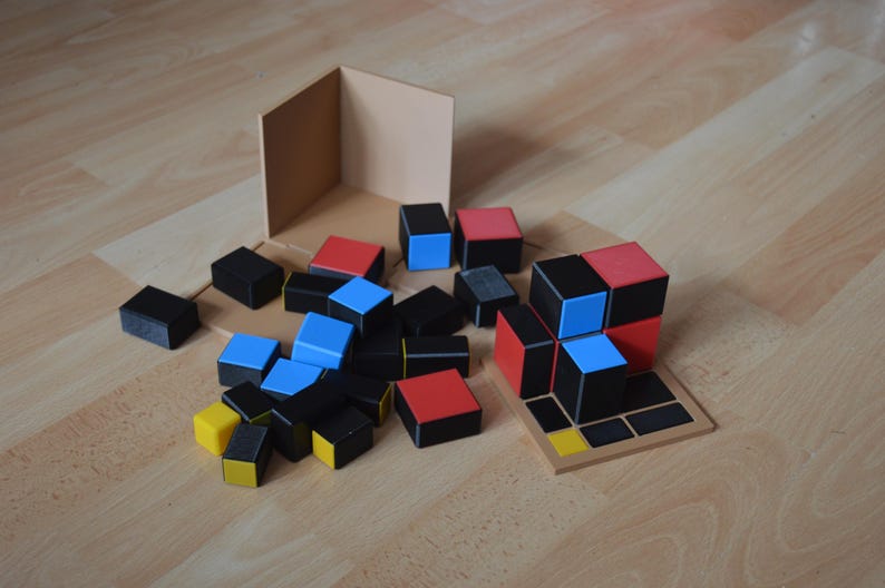 May include: A set of colourful wooden blocks in red, blue, black, and yellow. The blocks are arranged in a random pattern on a wooden surface. There is a wooden box in the background.