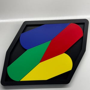 Op de afbeelding: Een geometrische puzzel met vier stukken in een zwart frame. De stukken zijn gevormd als gebogen rechthoeken en zijn rood, blauw, groen en geel gekleurd.