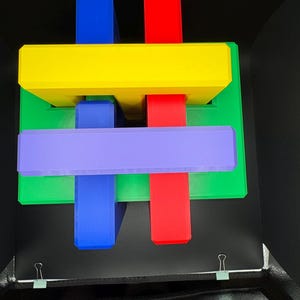 May include: A colorful wooden puzzle with interlocking pieces in red, yellow, green, blue, and purple. The puzzle is arranged in a cross shape.