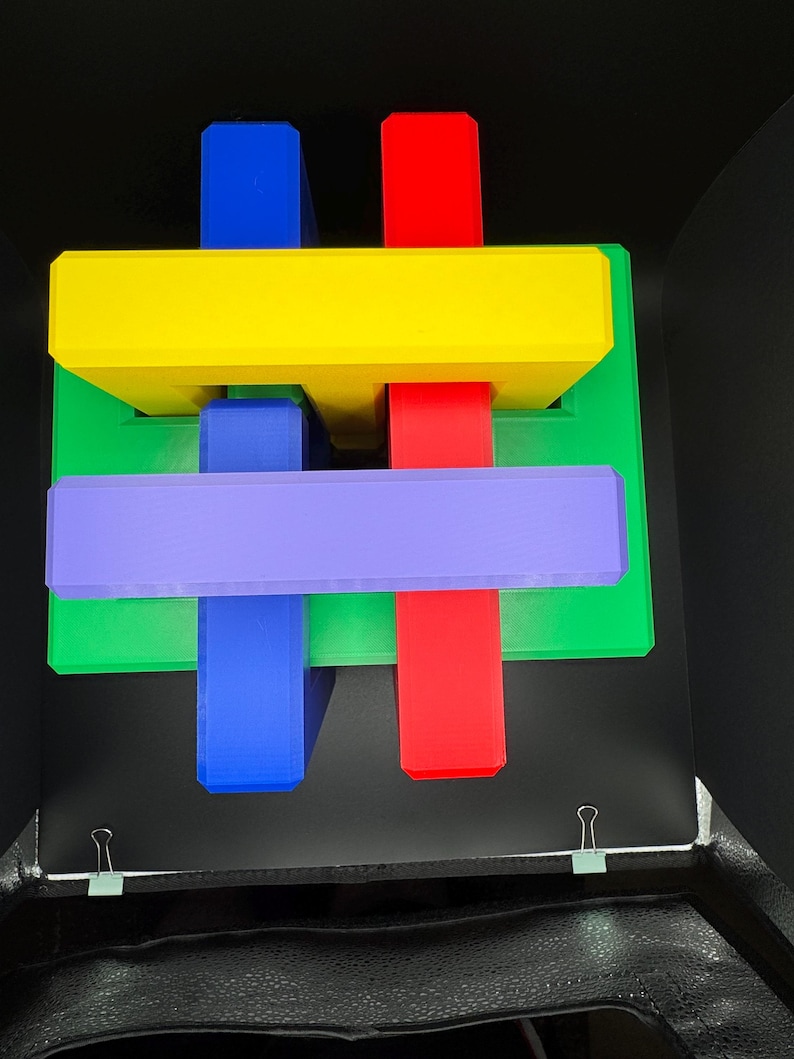 May include: A colorful wooden puzzle with interlocking pieces in red, yellow, green, blue, and purple. The puzzle is arranged in a cross shape.