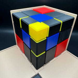 May include: A 3x3 cube puzzle with black, red, blue, and yellow squares. The cube is assembled in a pattern with the colours alternating.