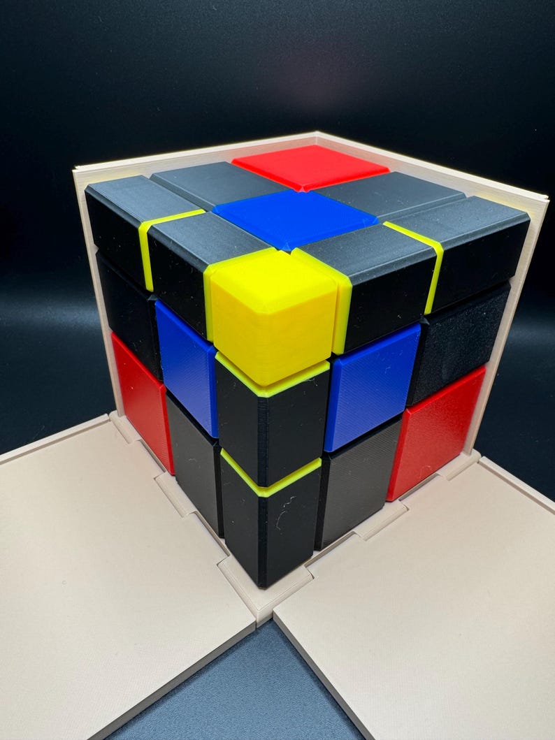 May include: A 3x3 cube puzzle with black, red, blue, and yellow squares. The cube is assembled in a pattern with the colours alternating.