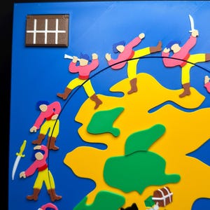 May include: A colorful, 3D-printed map with a blue background and a yellow landmass. Figures in pink shirts and yellow pants are depicted in action, some with swords. Green islands and a treasure chest are also visible.