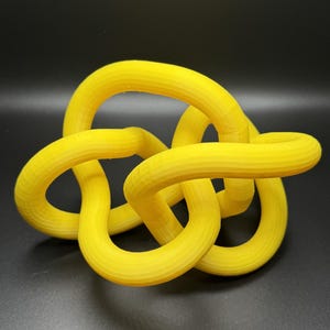 K&ouml;nnte beinhalten: Eine gelbe, 3D-gedruckte Knotenskulptur. Der Knoten besteht aus einem einzigen, durchgehenden St&uuml;ck Plastik und ist als Dekorationsobjekt konzipiert.