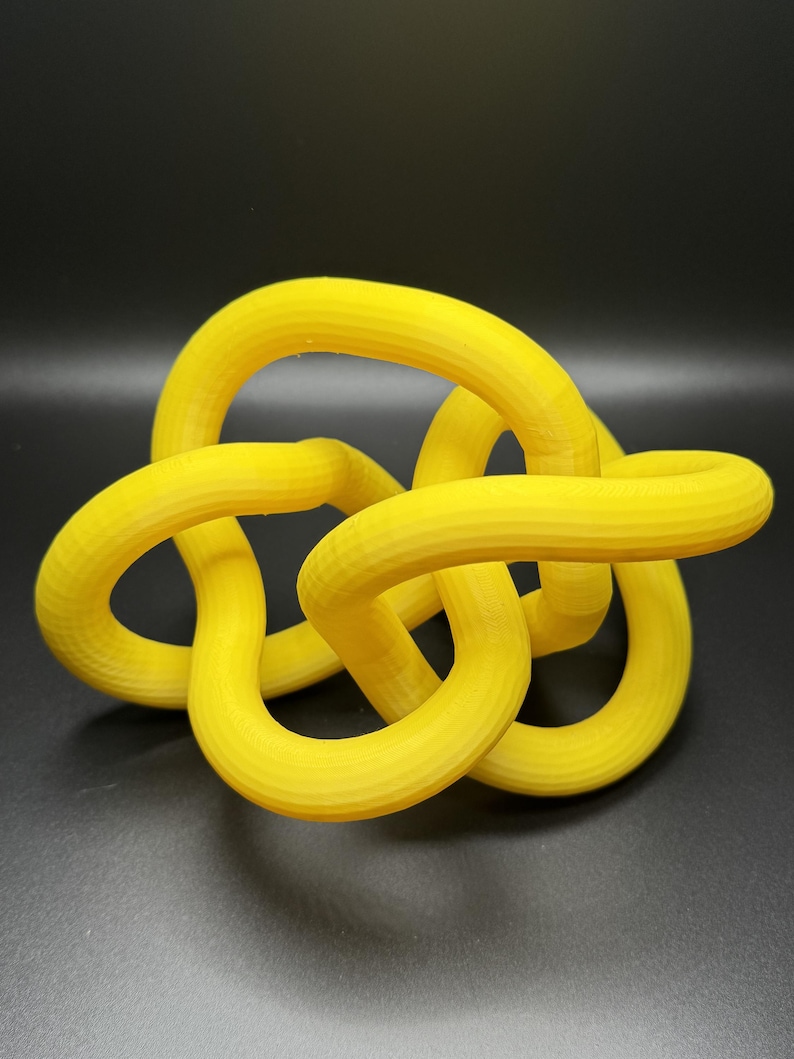 K&ouml;nnte beinhalten: Eine gelbe, 3D-gedruckte Knotenskulptur. Der Knoten besteht aus einem einzigen, durchgehenden St&uuml;ck Plastik und ist als Dekorationsobjekt konzipiert.