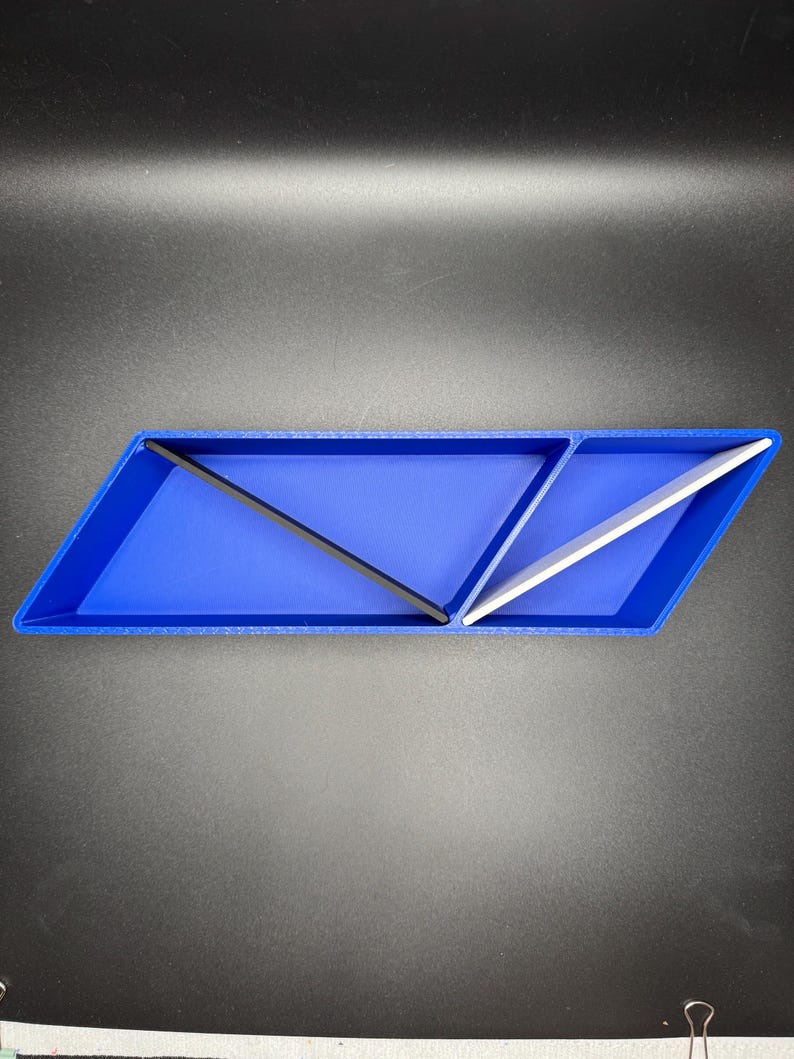 May include: A blue, triangular-shaped desktop organizer with two compartments. One compartment has a black divider and the other has a white divider.