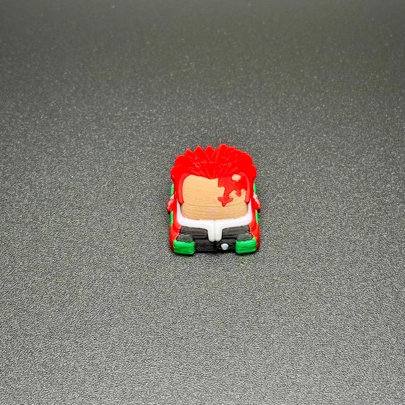 May include: A red and green keycap with a cartoon character design. The character has red hair, a white face, and a black and white outfit.