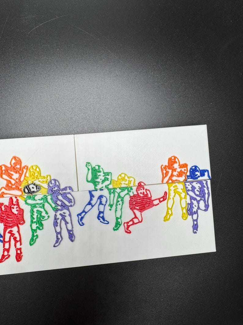 Pu&ograve; includere: Una carta bianca con un design arcobaleno di giocatori di football. I giocatori sono in varie pose, tra cui correre, calciare e lanciare la palla. La carta &egrave; divisa in due sezioni, con i giocatori sul lato sinistro della carta in un motivo arcobaleno dal rosso al viola, e i giocatori sul lato destro della carta in un motivo arcobaleno dal viola al rosso.