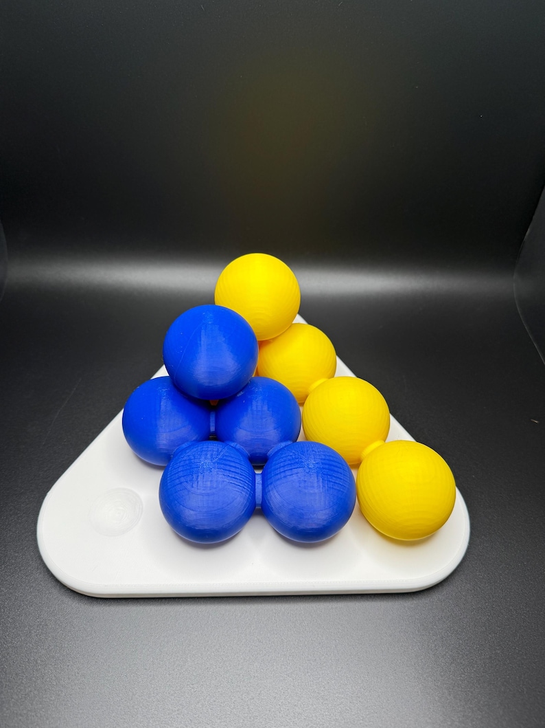 May include: A triangular puzzle game with blue and yellow balls. The balls are arranged in a pyramid shape on a white base.