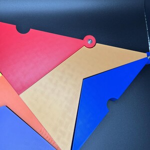 Peut inclure: Une &oelig;uvre d'art abstraite compos&eacute;e de formes triangulaires imbriqu&eacute;es de couleurs rouge, orange, beige, bleu et vert. Chaque pi&egrave;ce est reli&eacute;e par une attache argent&eacute;e. Le design est moderne et g&eacute;om&eacute;trique.