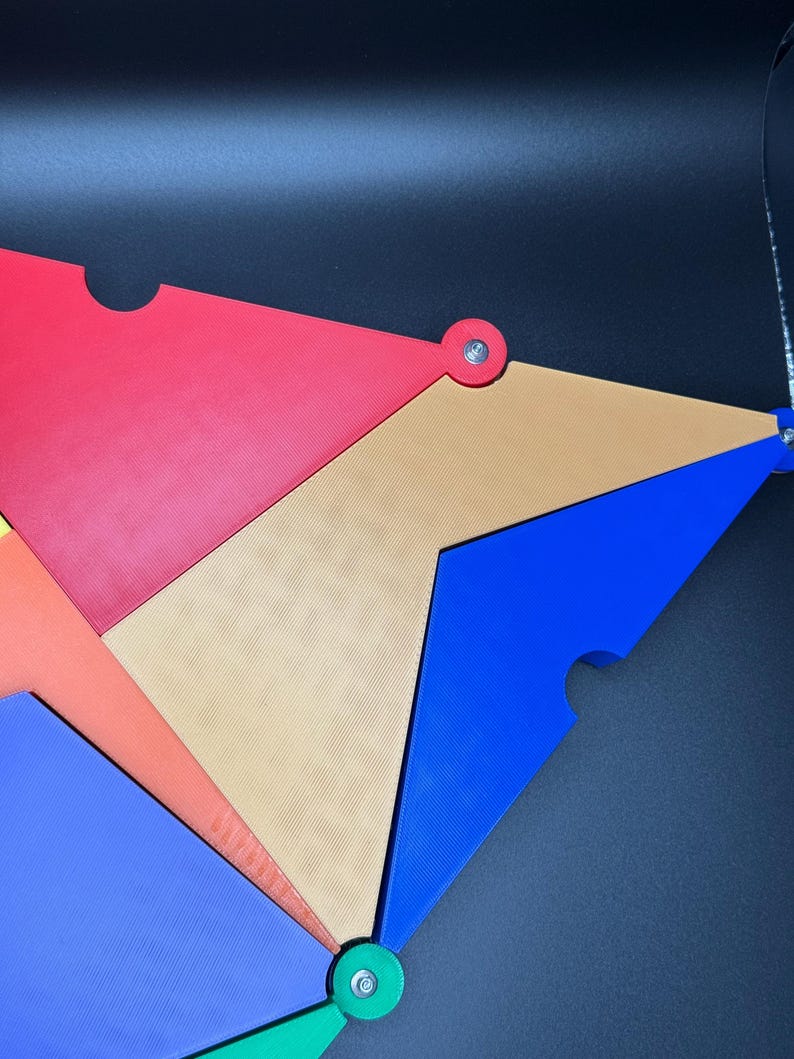 Peut inclure: Une &oelig;uvre d'art abstraite compos&eacute;e de formes triangulaires imbriqu&eacute;es de couleurs rouge, orange, beige, bleu et vert. Chaque pi&egrave;ce est reli&eacute;e par une attache argent&eacute;e. Le design est moderne et g&eacute;om&eacute;trique.