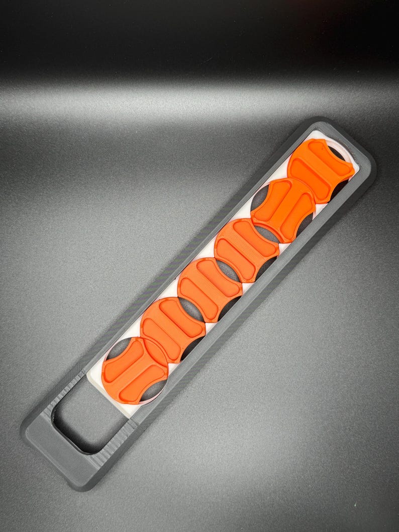 May include: A black plastic holder with a row of six orange round buttons. The holder has a handle on one end.