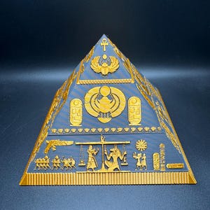 Puede incluir: Una pir&aacute;mide azul y dorada con intrincados dise&ntilde;os jerogl&iacute;ficos egipcios. La pir&aacute;mide presenta tallas detalladas de faraones, dioses y s&iacute;mbolos. La base y los bordes son dorados, mientras que el cuerpo principal es azul.