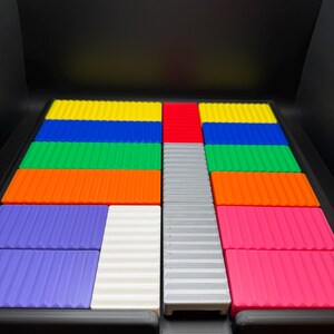 May include: A colorful puzzle game with rectangular pieces in various colors, including blue, green, orange, purple, white, gray, red, and pink. The pieces have a ridged texture and are arranged in a grid-like pattern.