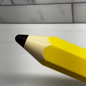May include: Close-up of a large yellow pencil with a black eraser. The pencil is made of a smooth, hard plastic.