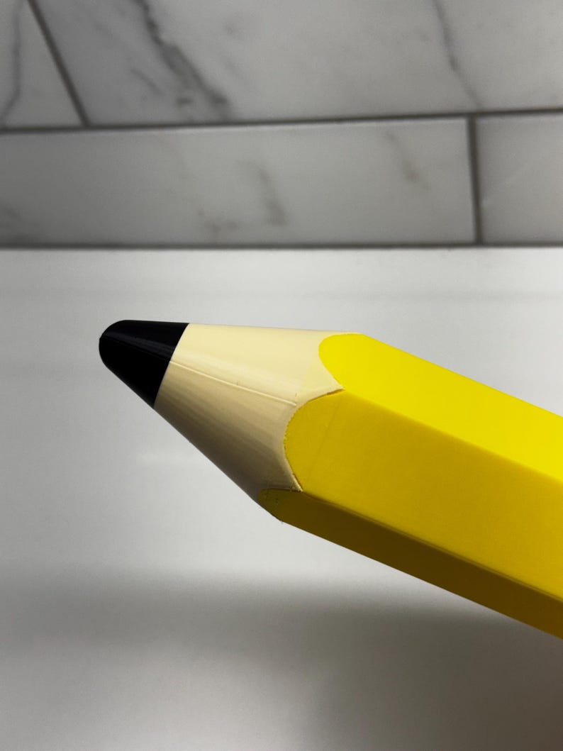 May include: Close-up of a large yellow pencil with a black eraser. The pencil is made of a smooth, hard plastic.
