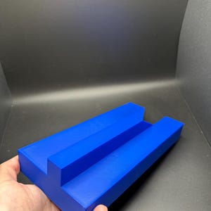 Può includere: Un organizzatore in plastica blu con due fessure. L'organizzatore è progettato per contenere oggetti come penne, matite o altri piccoli oggetti.