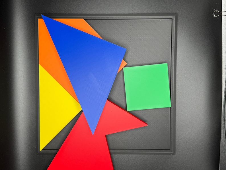 May include: A set of five colourful geometric shapes, including a blue triangle, a red triangle, a yellow triangle, an orange triangle, and a green square, arranged on a black surface.