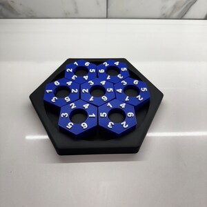 May include: A blue hexagonal puzzle with white numbers on each piece. The puzzle is made up of 12 pieces, each with a different number. The puzzle is arranged in a circle, with the numbers 1 through 12 in order.
