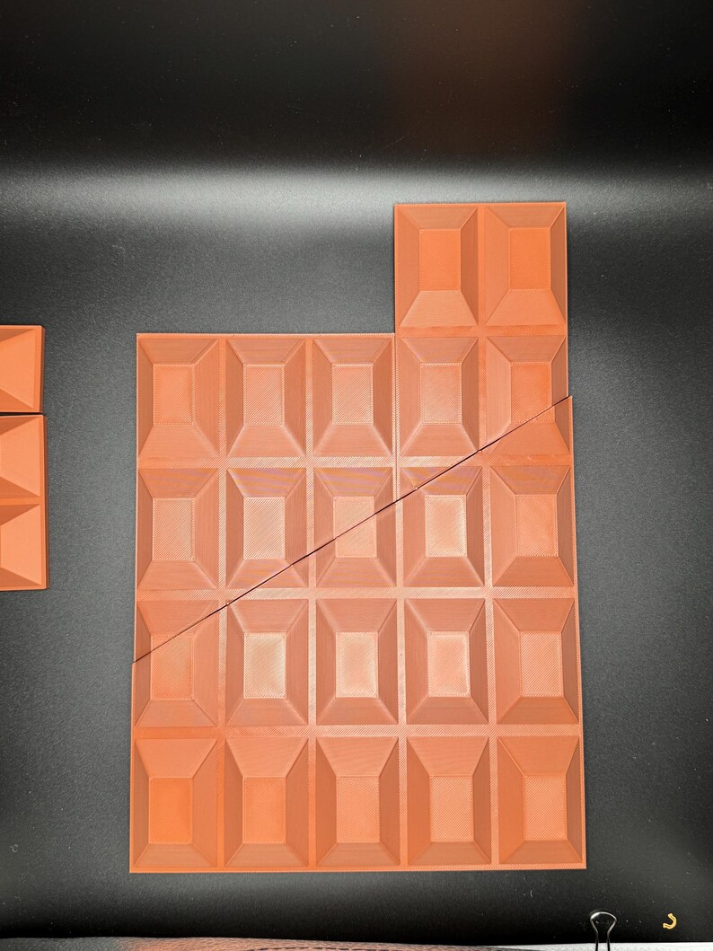 Op de afbeelding: Een grote, oranje-bruine chocolade reep met een getextureerd oppervlak, gebroken in meerdere stukken. De reep is gemaakt van een raster van vierkanten.