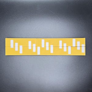 May include: A yellow ruler with white markings. The ruler is divided into sections with different lengths of white markings.